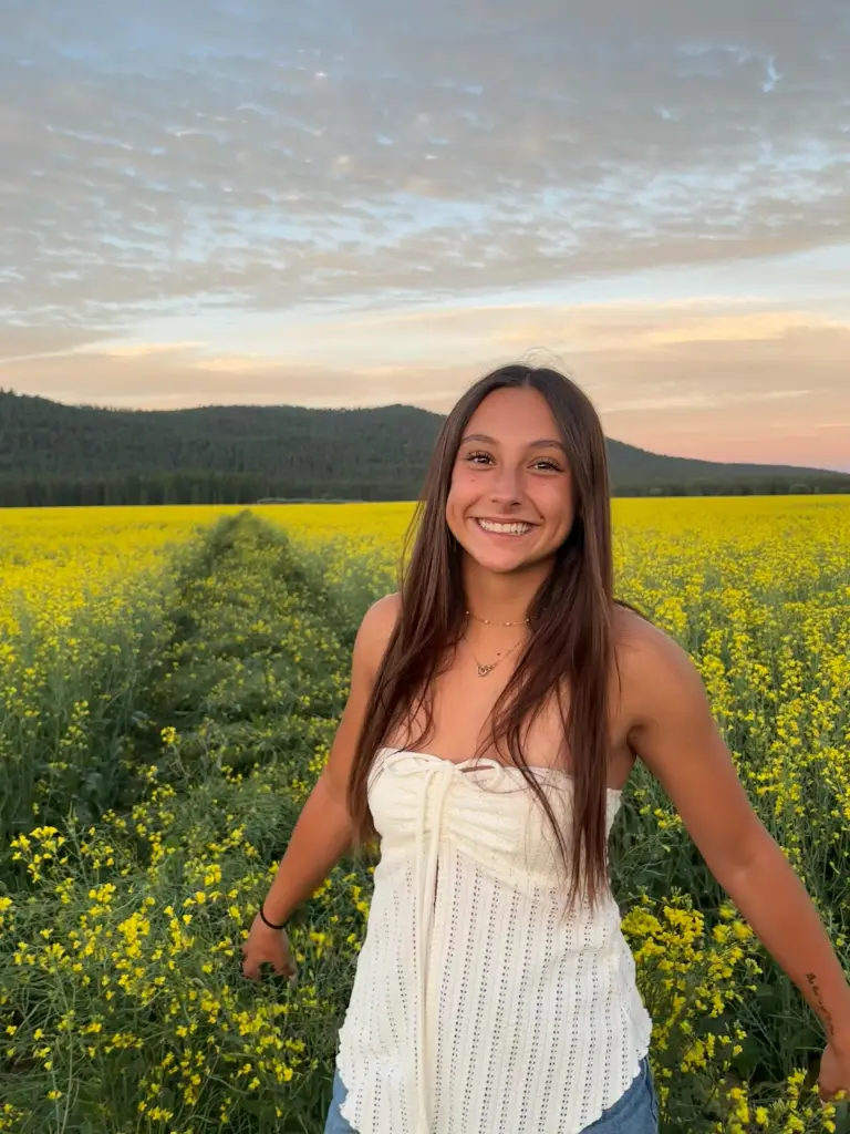 Samantha Rensvold standing in a field of yellow flowers during sunset.