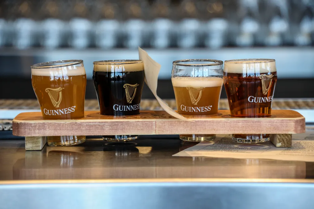Four glasses of Guinness beer arranged on a wooden flight board at a brewery.