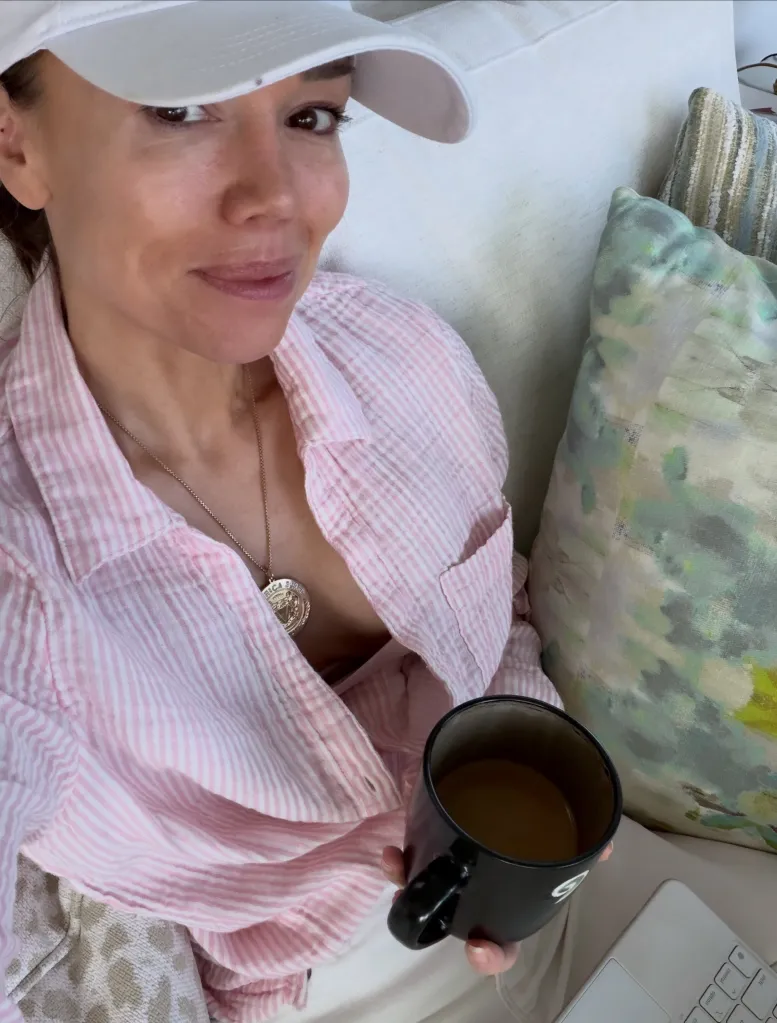 Sara Gore wearing a white cap and a pink-and-white striped shirt, holding a black mug of coffee on a couch.
