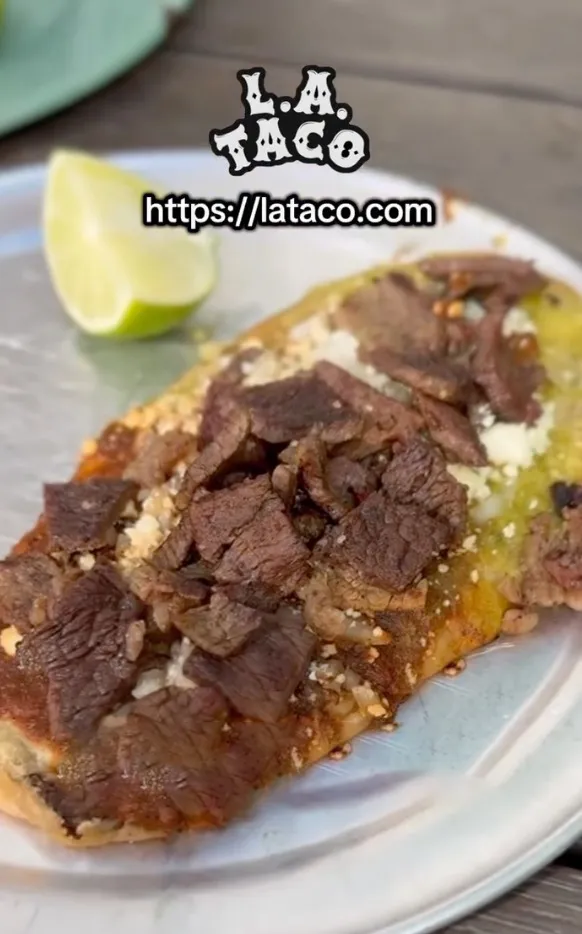 A plate with a Mexican dish, topped with meat, cheese, and lime.