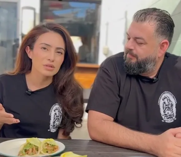 Sasha Renée Pérez and a man wearing matching LA Taco shirts seated at a table with tacos.