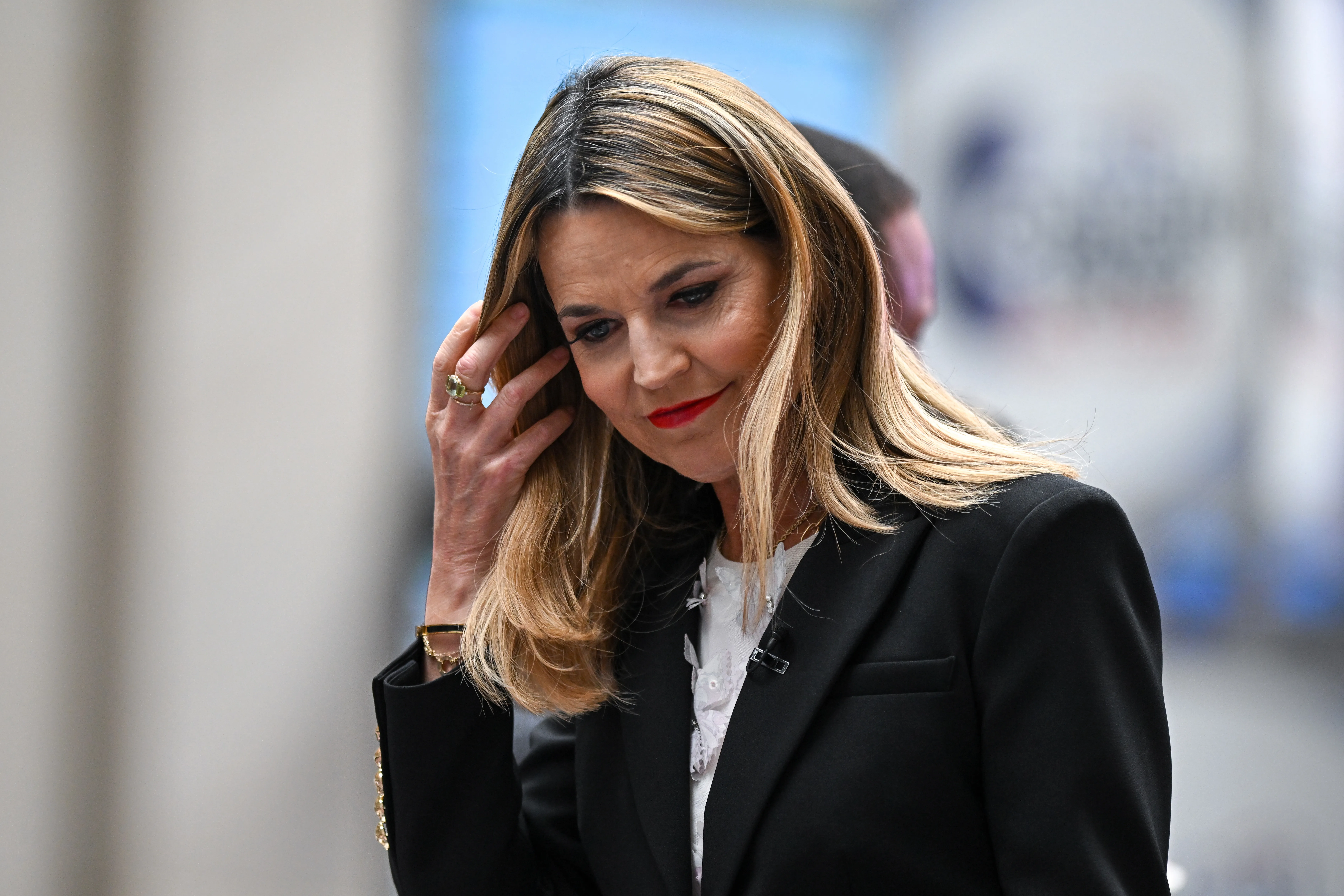 Savannah Guthrie adjusts her hair while wearing a black blazer.