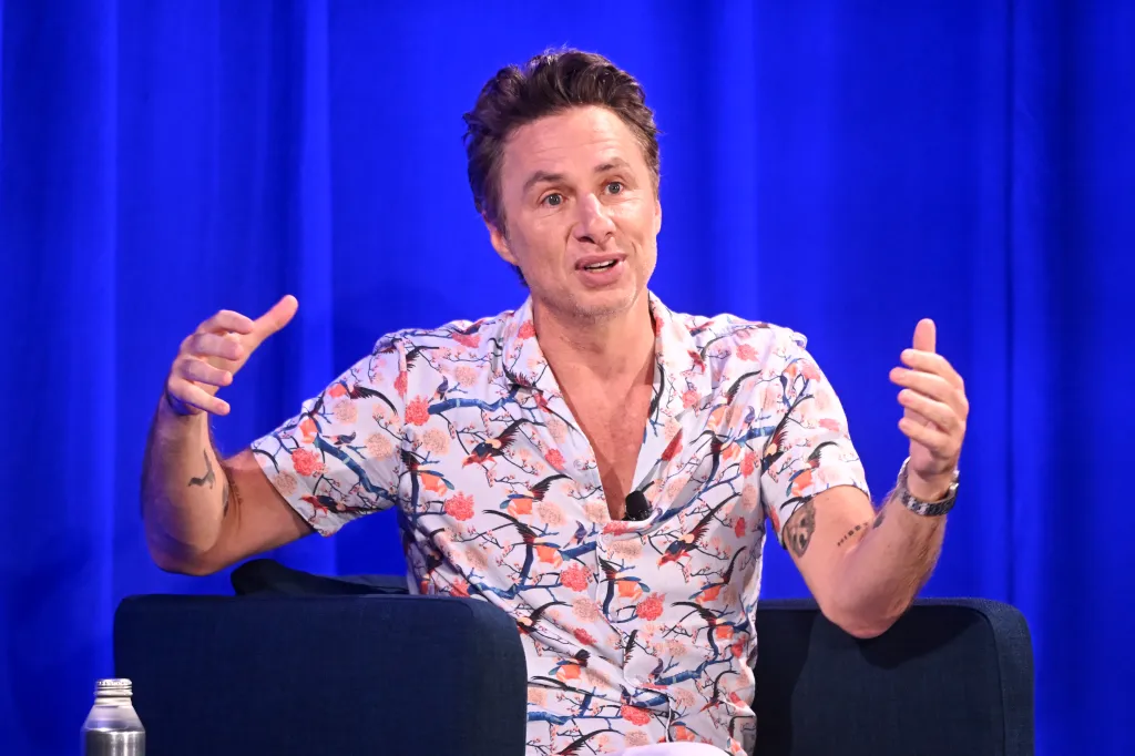 Zach Braff speaks at a panel event, gesturing with his hands.