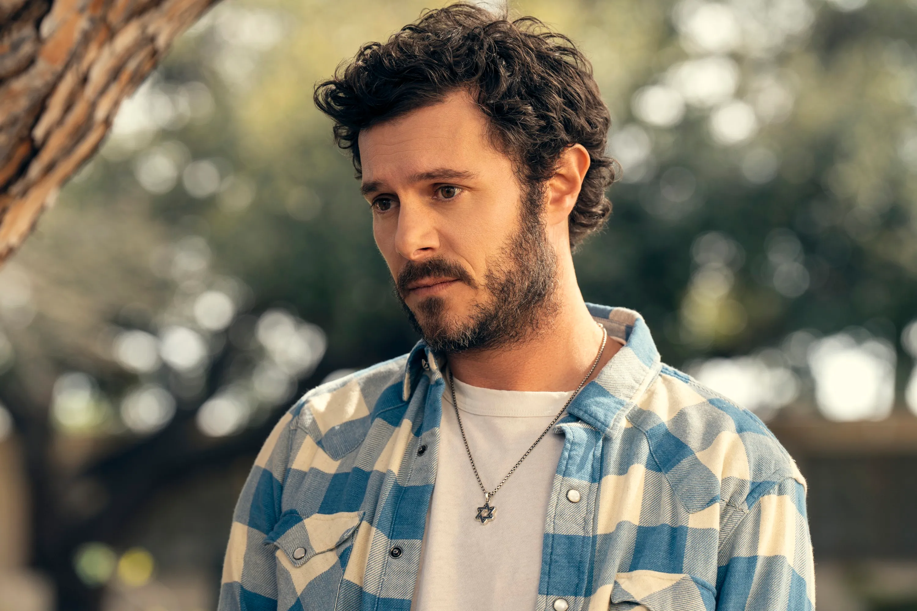 Adam Brody wearing a blue and white checkered shirt and a Star of David necklace.