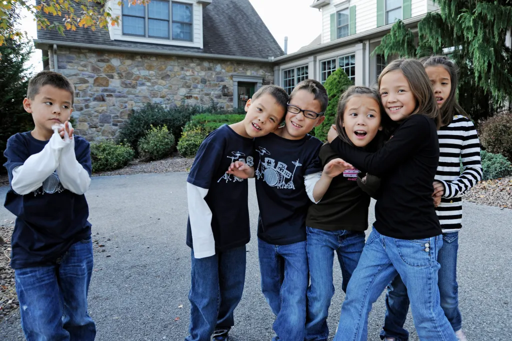 Six children posing together outdoors, with one boy standing slightly apart and looking away.