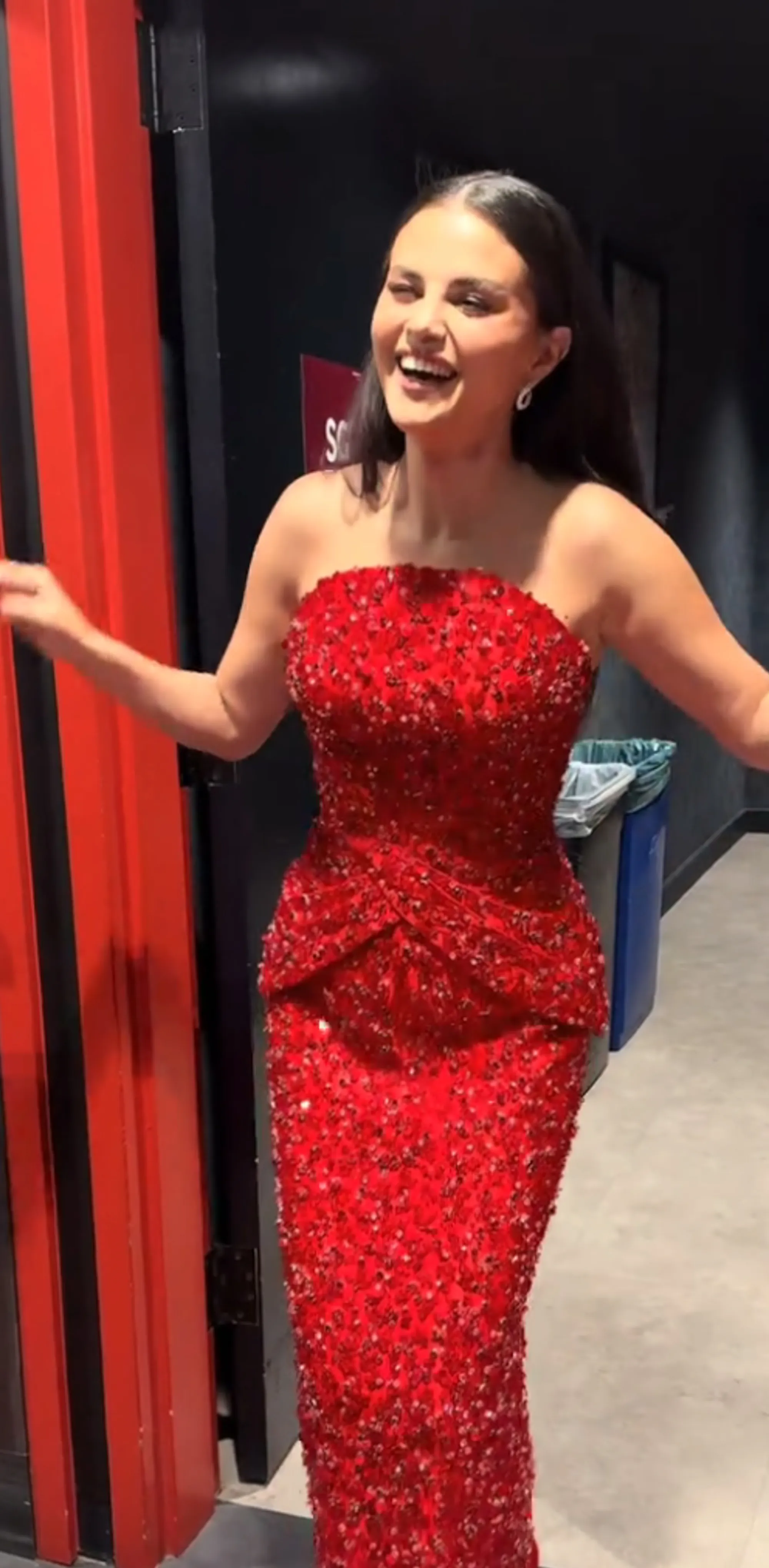 Selena Gomez smiling while wearing a red strapless dress.
