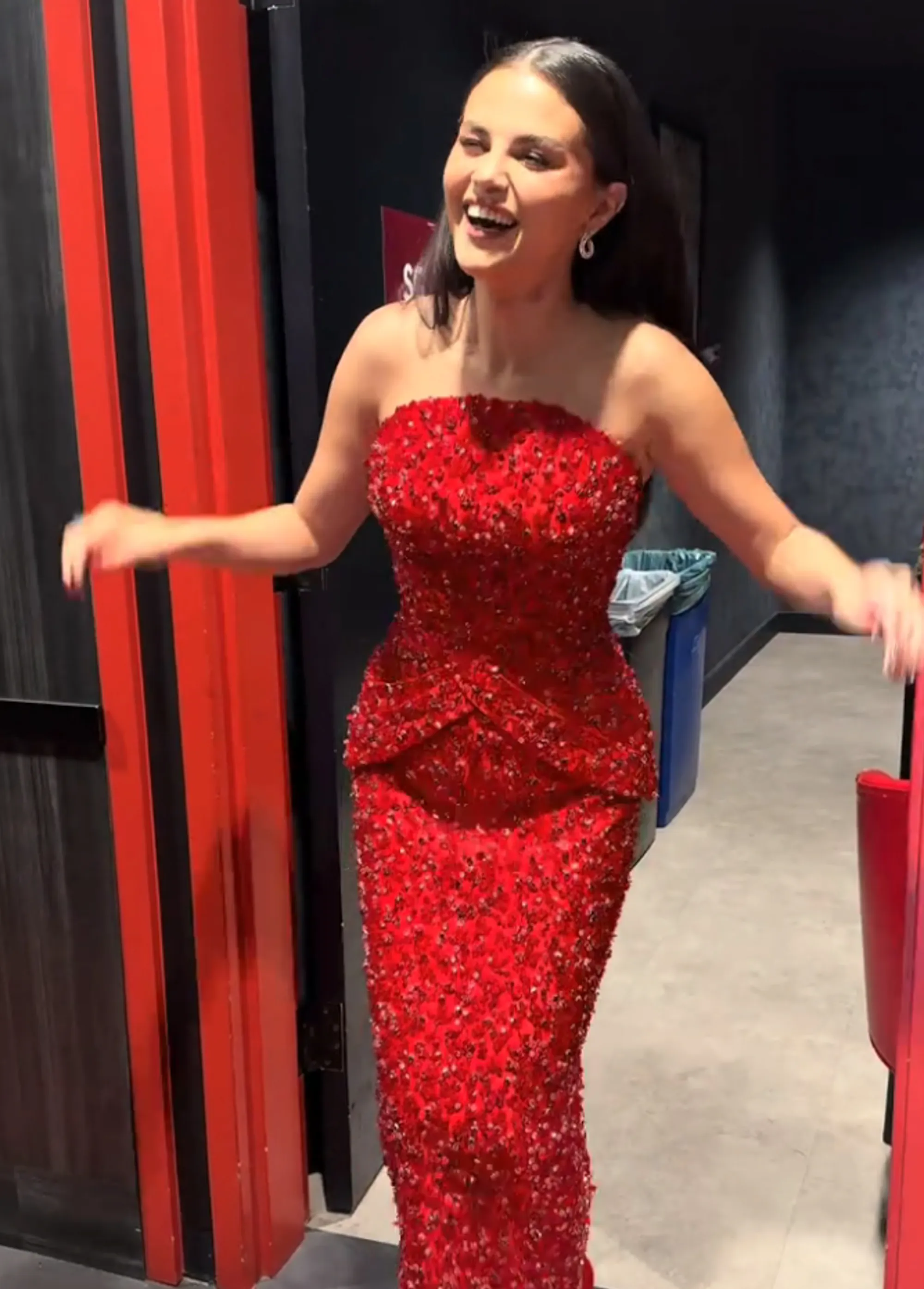 Selena Gomez wearing a sparkly red strapless dress and smiling.