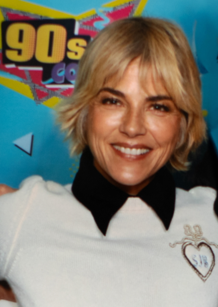 Selma Blair smiling in front of a 90s Con banner.