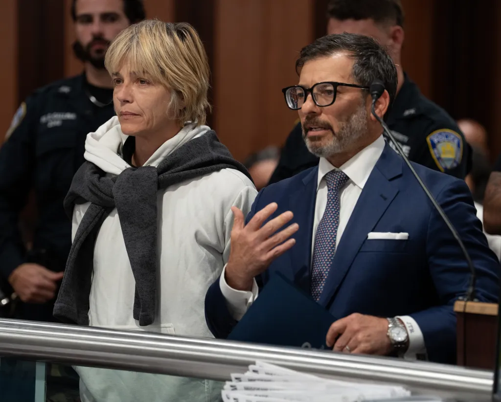 Selma Blair in a white hoodie stands in a courtroom with her attorney while police officers stand in the background.