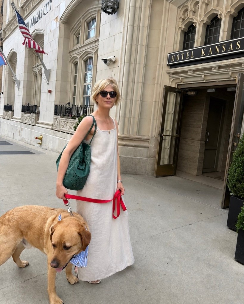 Selma Blair wearing a white dress and sunglasses, holding a red leash attached to a golden retriever outside the Hotel Kansas City.