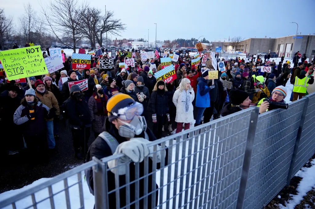 People protest outside a building in Minneapolis, holding signs against increased immigration enforcement.