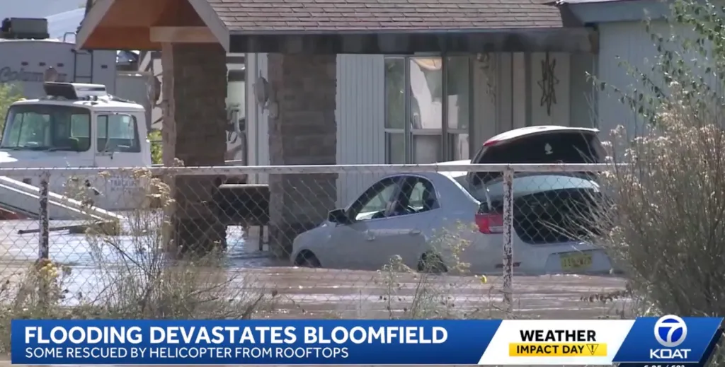 Severe flooding surrounds a house in Bloomfield, with floodwaters reaching up to the car and porch.