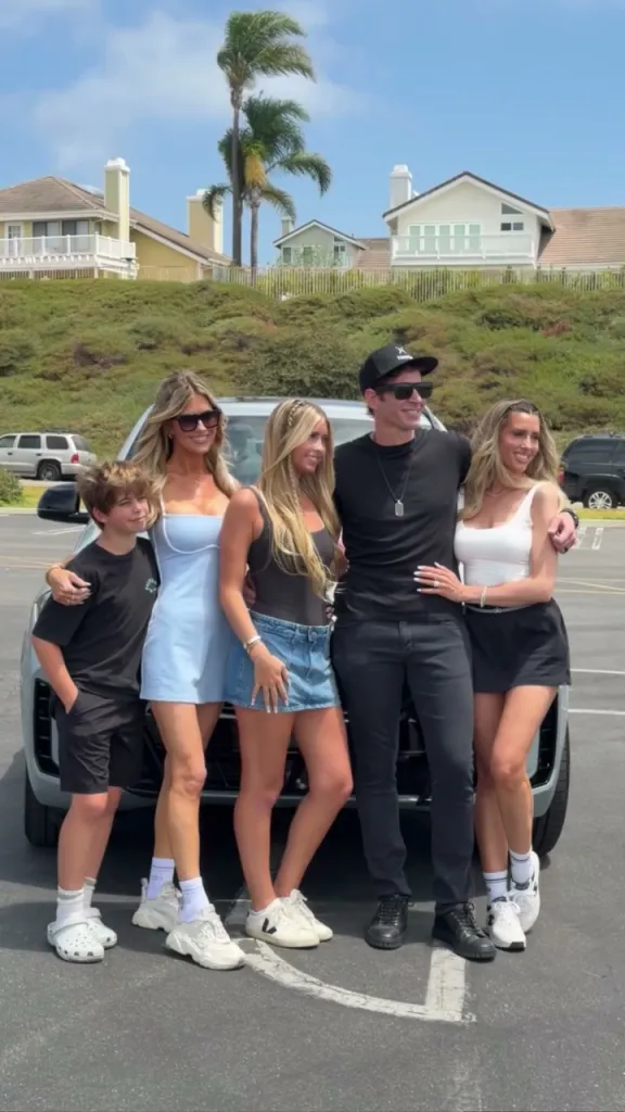 Tarek El Moussa and his family posing in front of a car.