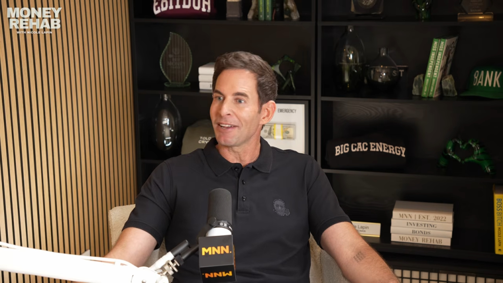 Tarek El Moussa sits in front of a bookshelf with a microphone in front of him for the podcast Money Rehab.