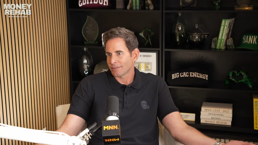 Tarek El Moussa sits in front of a bookshelf in a studio, speaking into a microphone.