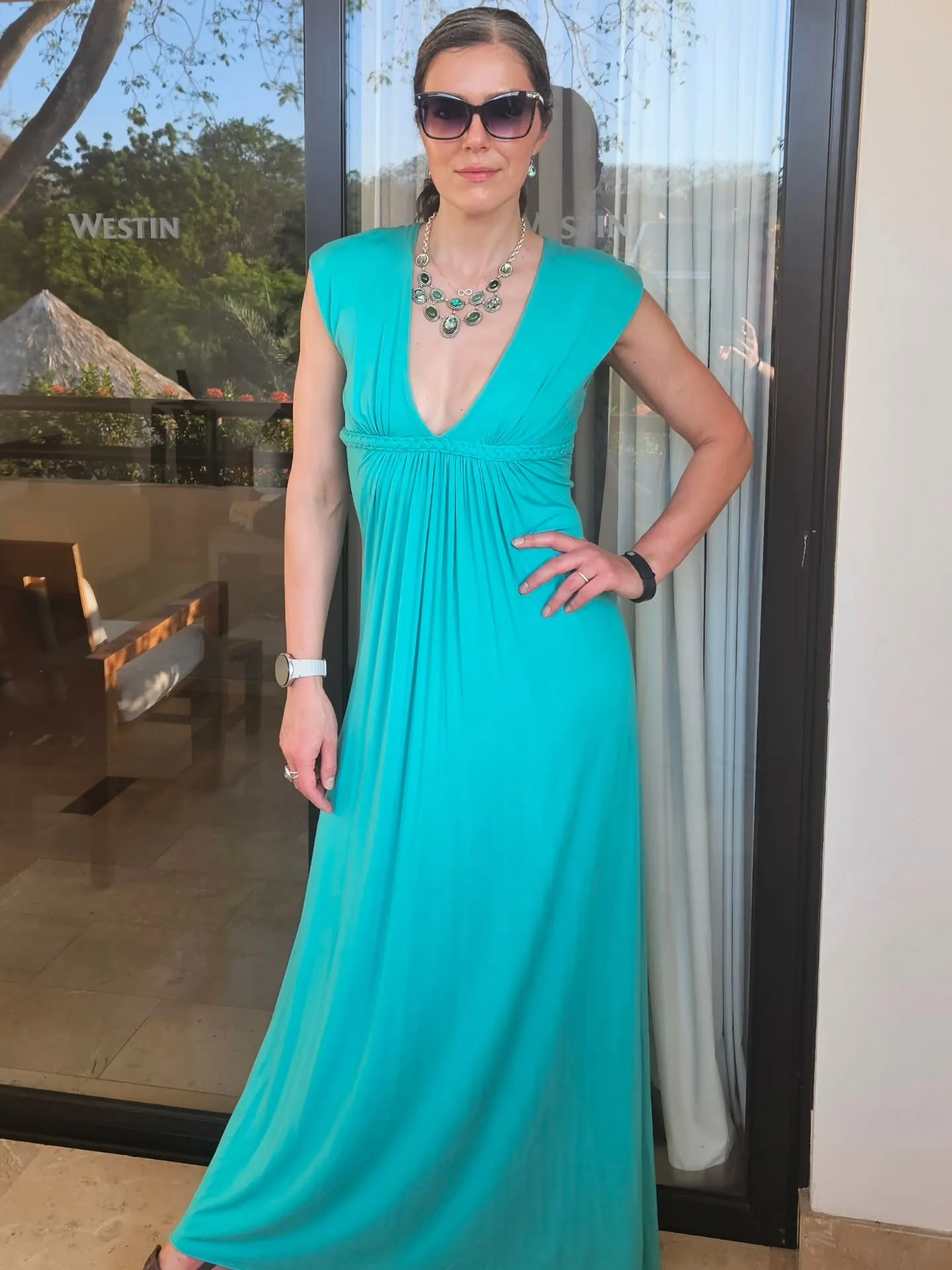 Adrianne Curry poses in a turquoise dress and sunglasses.