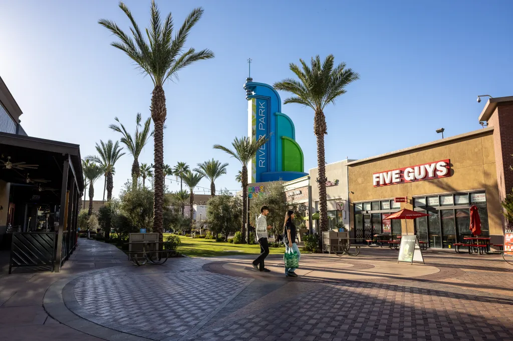 Shoppers walk among palm trees surrounding the River Park shopping center.