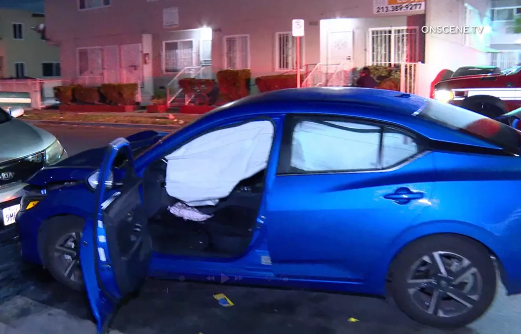 A damaged blue car with deployed airbags parked on a street at night after a hit-and-run crash.