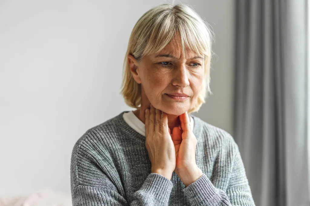 An elderly woman with a sore throat touching her neck.