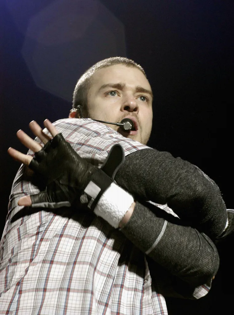 Justin Timberlake performing live on stage with a headset microphone and a black glove.