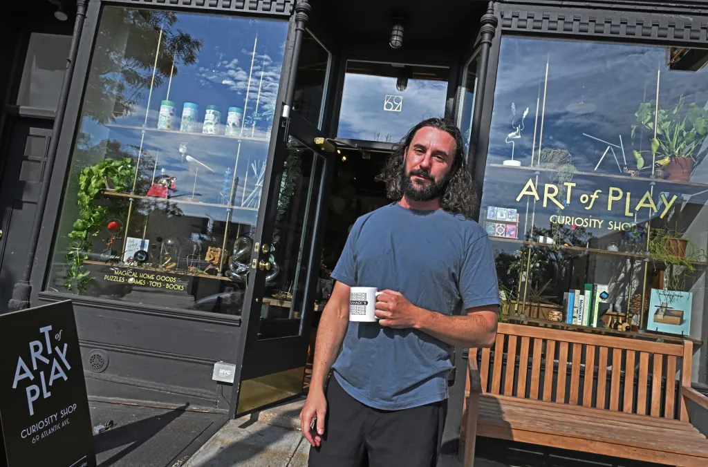 Adam Rubin, the owner of the Art of Play store in Brooklyn Heights, holding a mug outside his shop.