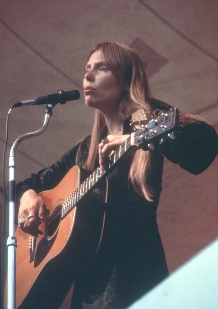 Singer-songwriter Joni Mitchell performs while playing an acoustic guitar.