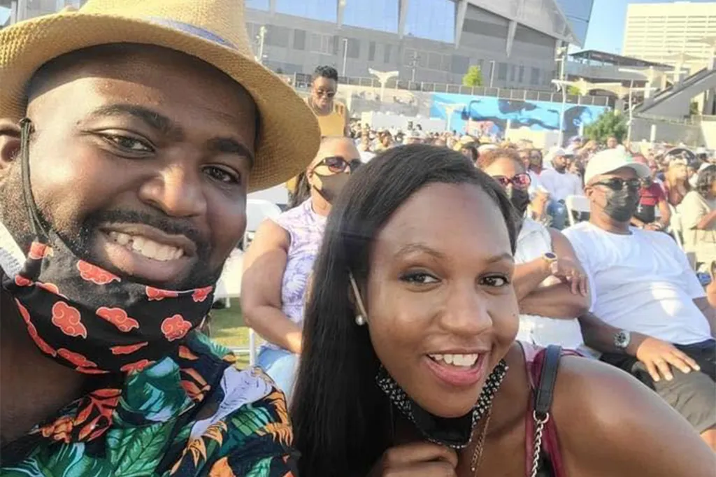 A man and woman smiling for a selfie at an outdoor event with a crowd in the background.