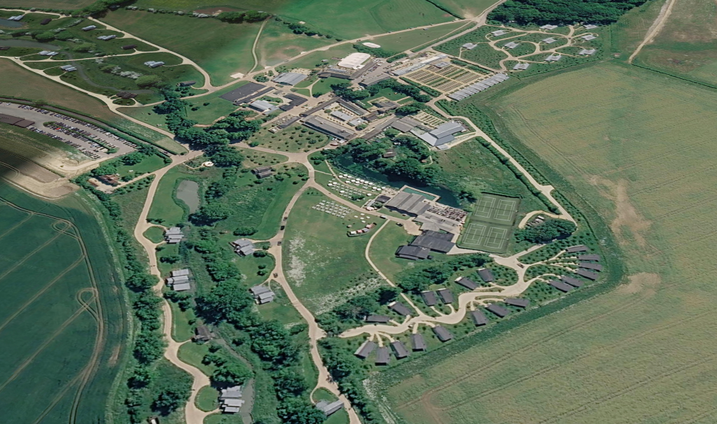 Aerial view of Soho Farmhouse, showing its sprawling countryside estate layout, including main buildings, cabins, and surrounding fields.