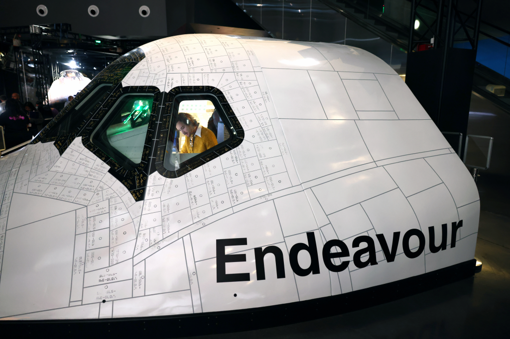 Close-up view of the massive main engines and underside of the Space Shuttle Endeavour on display at the Samuel Oschin Air and Space Center, with visitors walking underneath.