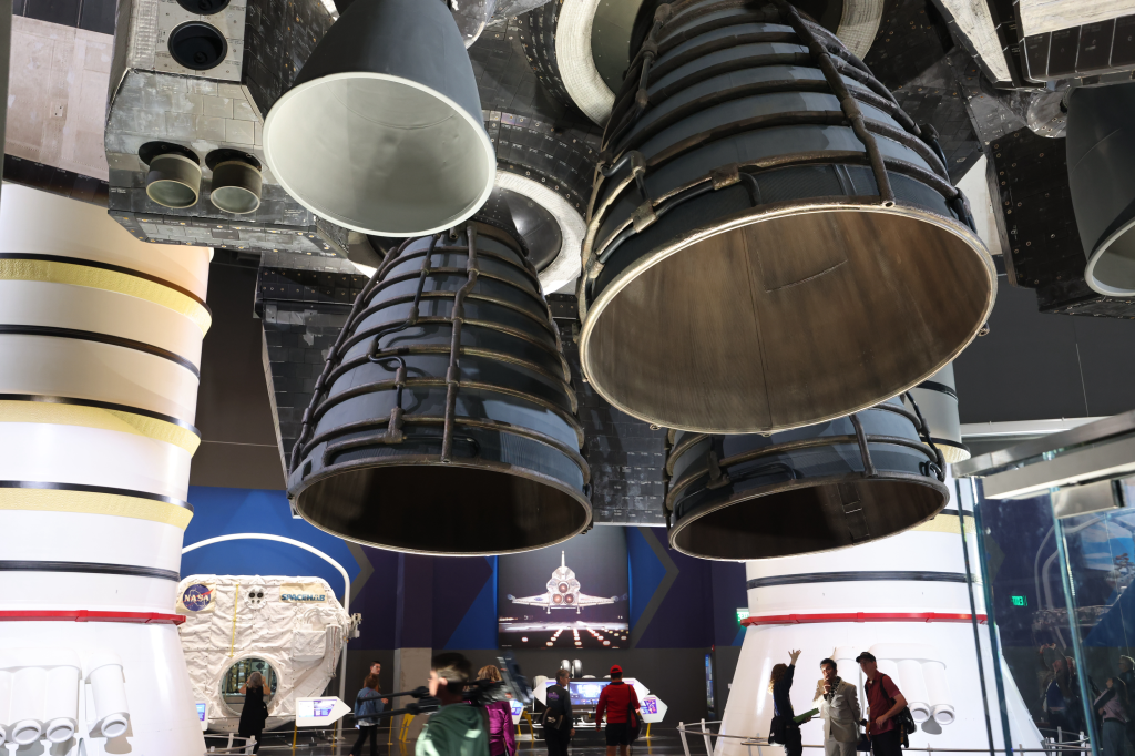 Close-up view of the massive main engines and underside of the Space Shuttle Endeavour on display at the Samuel Oschin Air and Space Center, with visitors walking underneath.
