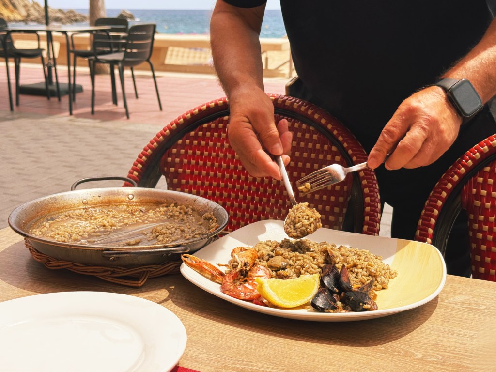 A waiter serves seafood paella at a restaurant by the Mediterranean Sea.