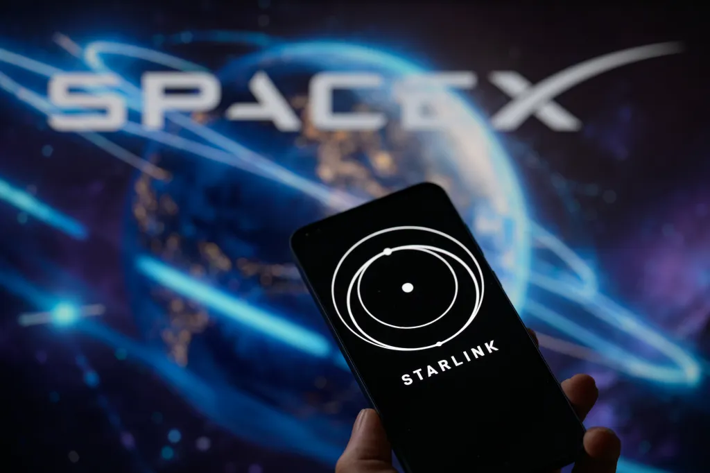 Photo illustration of the Starlink logo displayed on a mobile phone with the SpaceX logo and Earth in the background.