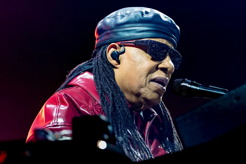 Stevie Wonder performs live on stage, wearing a leather cap and jacket, while singing into a microphone.