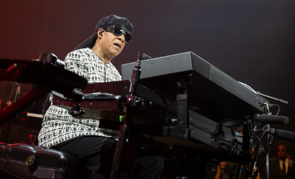 Stevie Wonder performs on the opening night of his tour, playing the keyboard in a black and white patterned jacket and cap.
