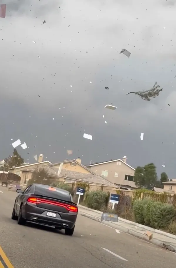 Strong swirling winds sweep through a Victorville neighborhood, lifting debris into the air above a car on the road.