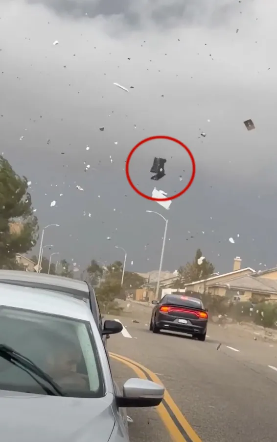 Strong swirling winds lift a trash bin into the air above a neighborhood street.
