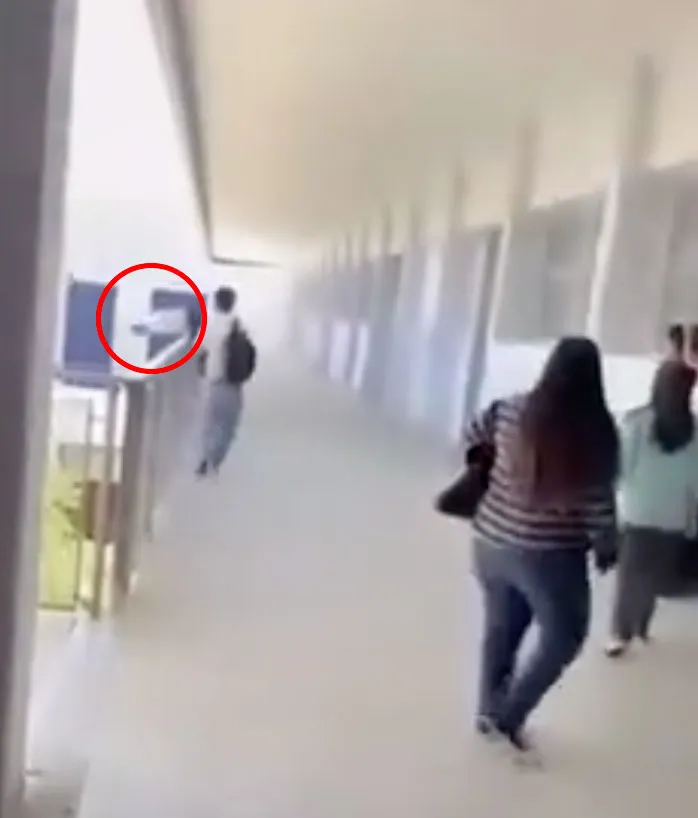 A student running down a high school hallway, with a red circle highlighting a person near a balcony railing.