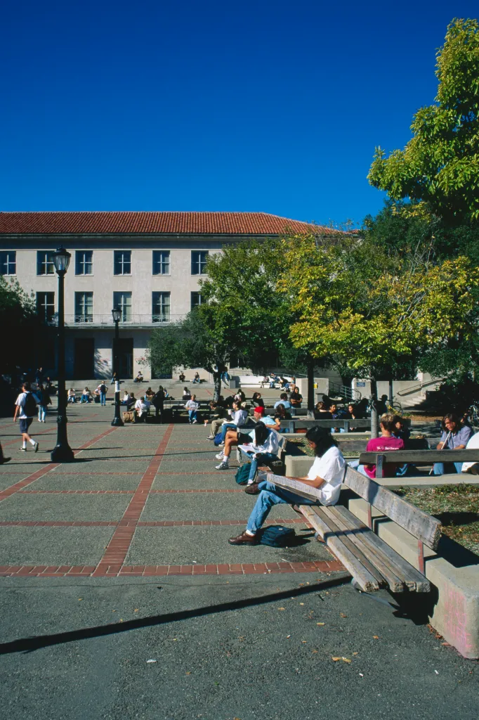 Students relaxing and reading on benches in a public square on the University of California campus.