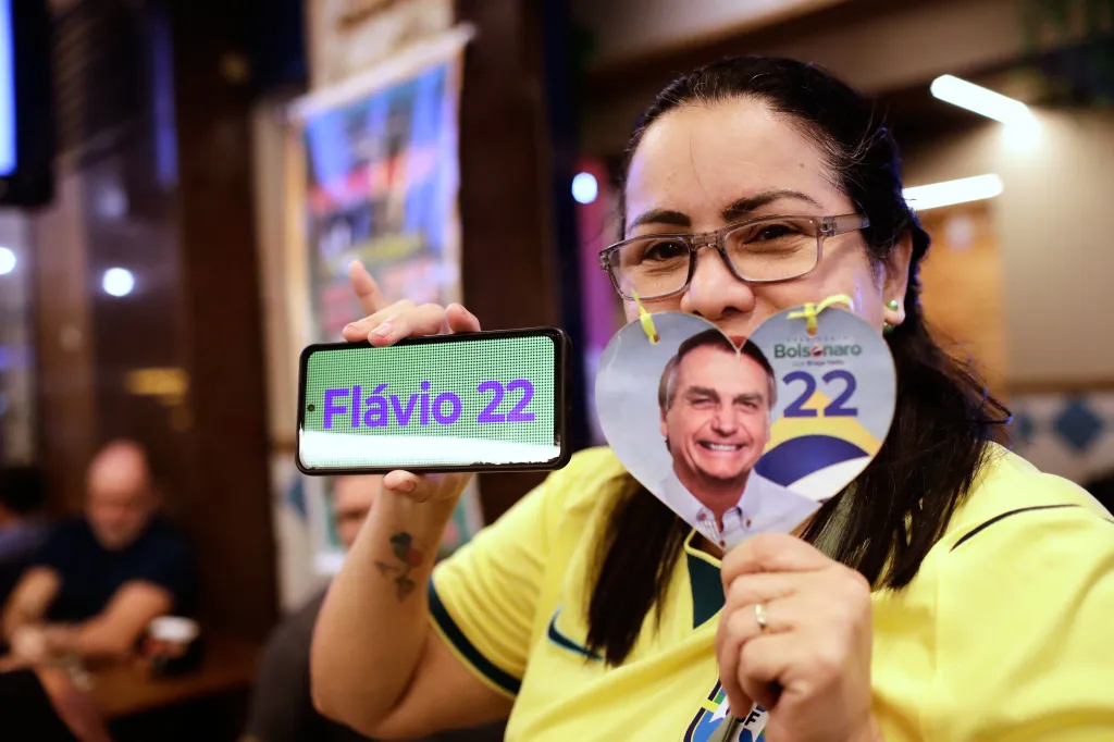 A supporter of presidential candidate Flavio Bolsonaro poses with a phone displaying his name and number alongside a heart-shaped sign with his face.