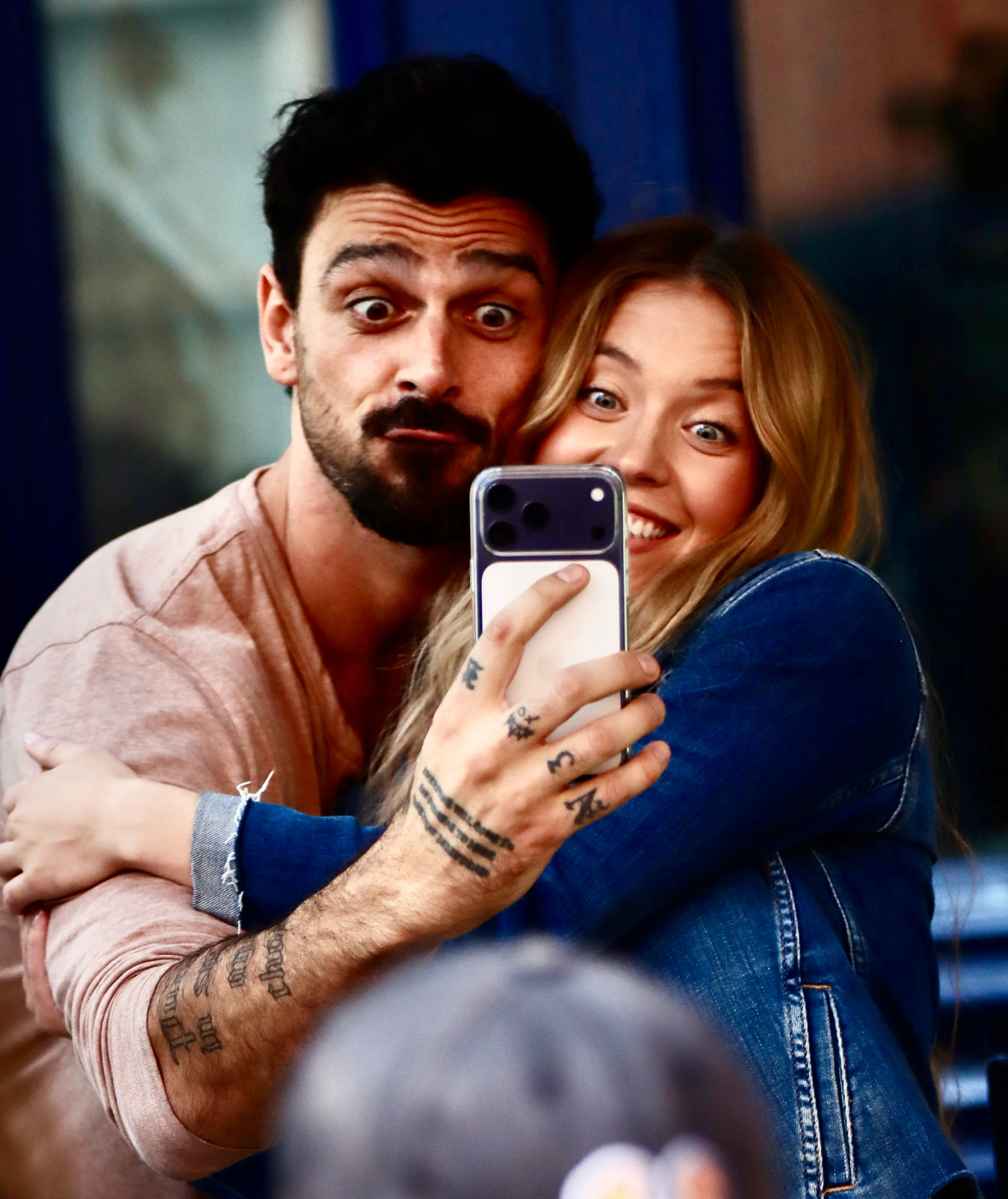 Sydney Sweeney and Michele Morrone take a playful selfie together on a film set, with Morrone making a funny face and Sweeney smiling widely.