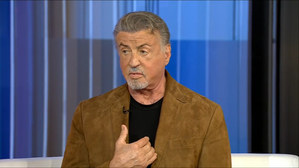 Sylvester Stallone sitting in front of a blue background.