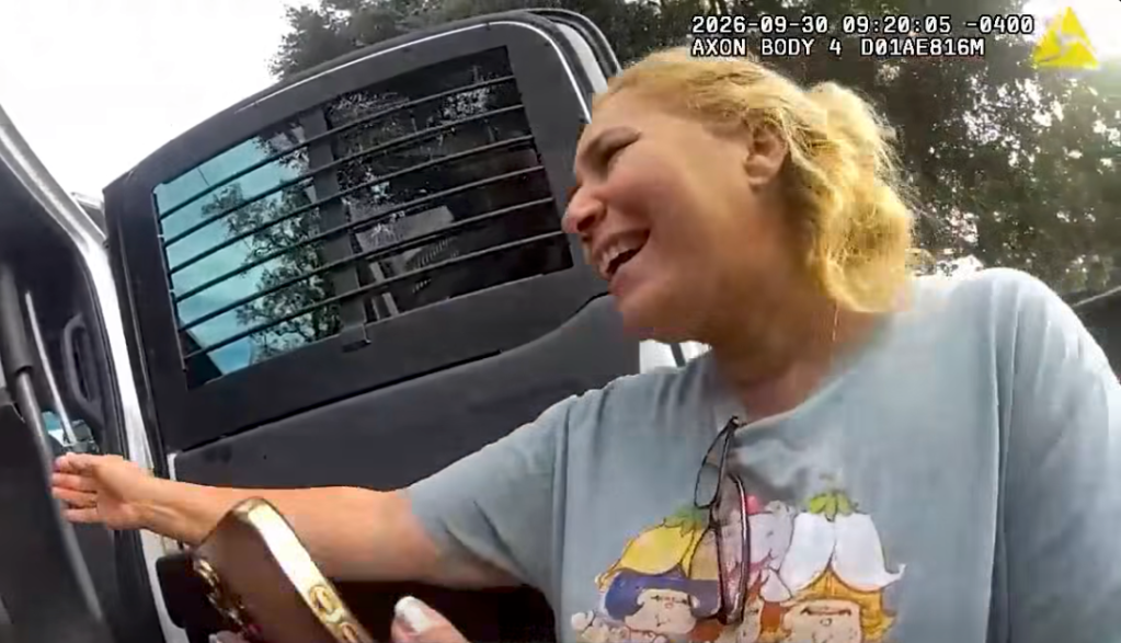 Body-worn camera footage of a blonde woman laughing and looking into the back of a police vehicle.
