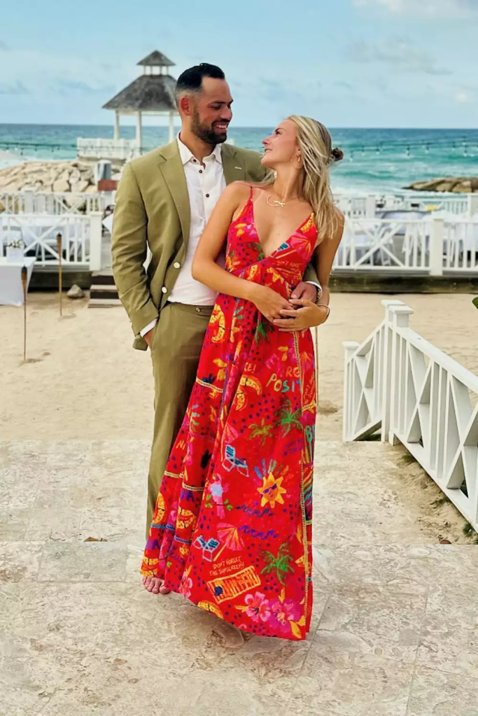 Taylor Ann Green and Gaston Rojas standing together outdoors near a beach, looking at each other and smiling.