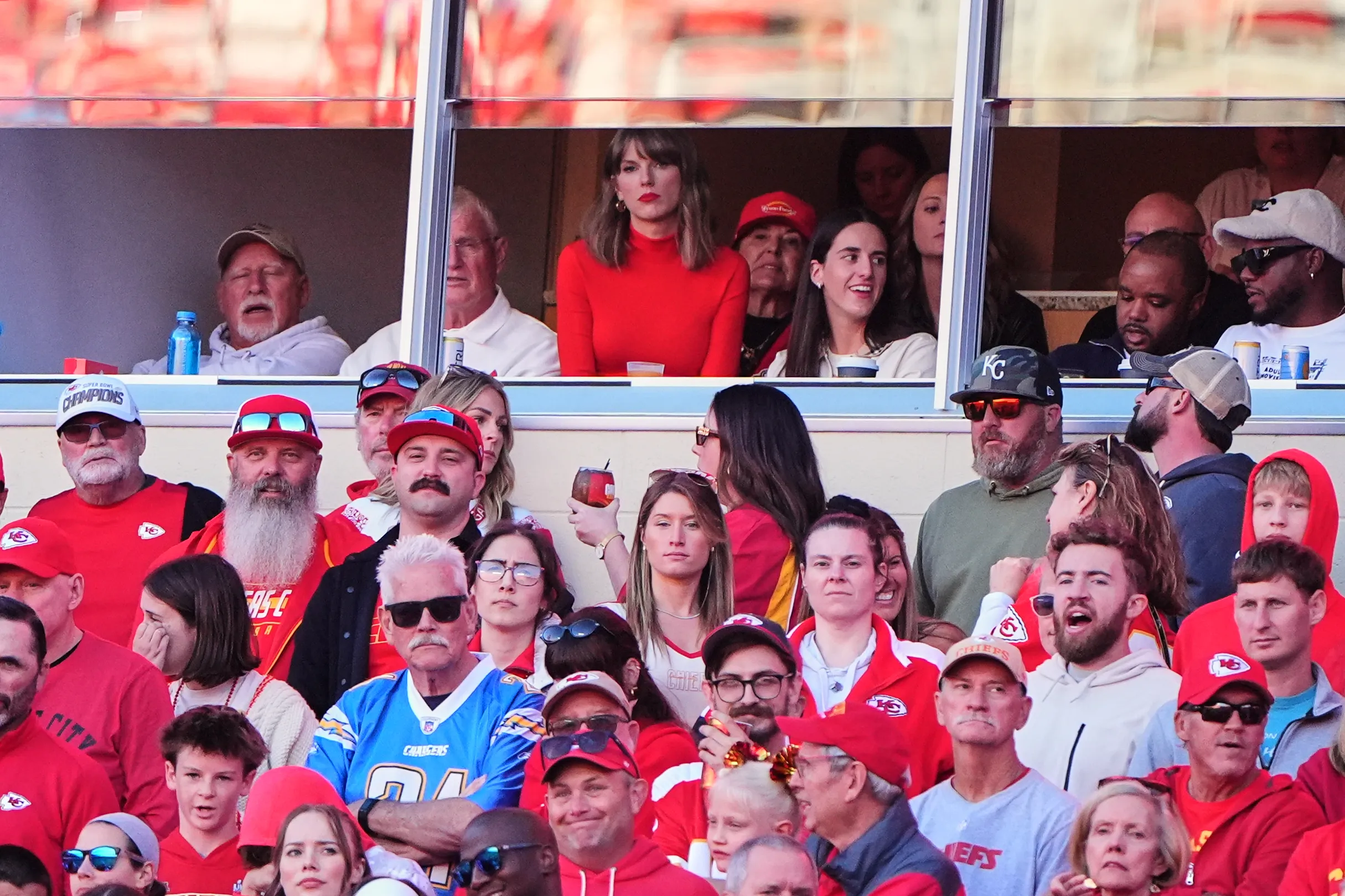 Taylor Swift, center, and WNBA player Caitlin Clark, center right, sit in a suite watching an NFL football game.