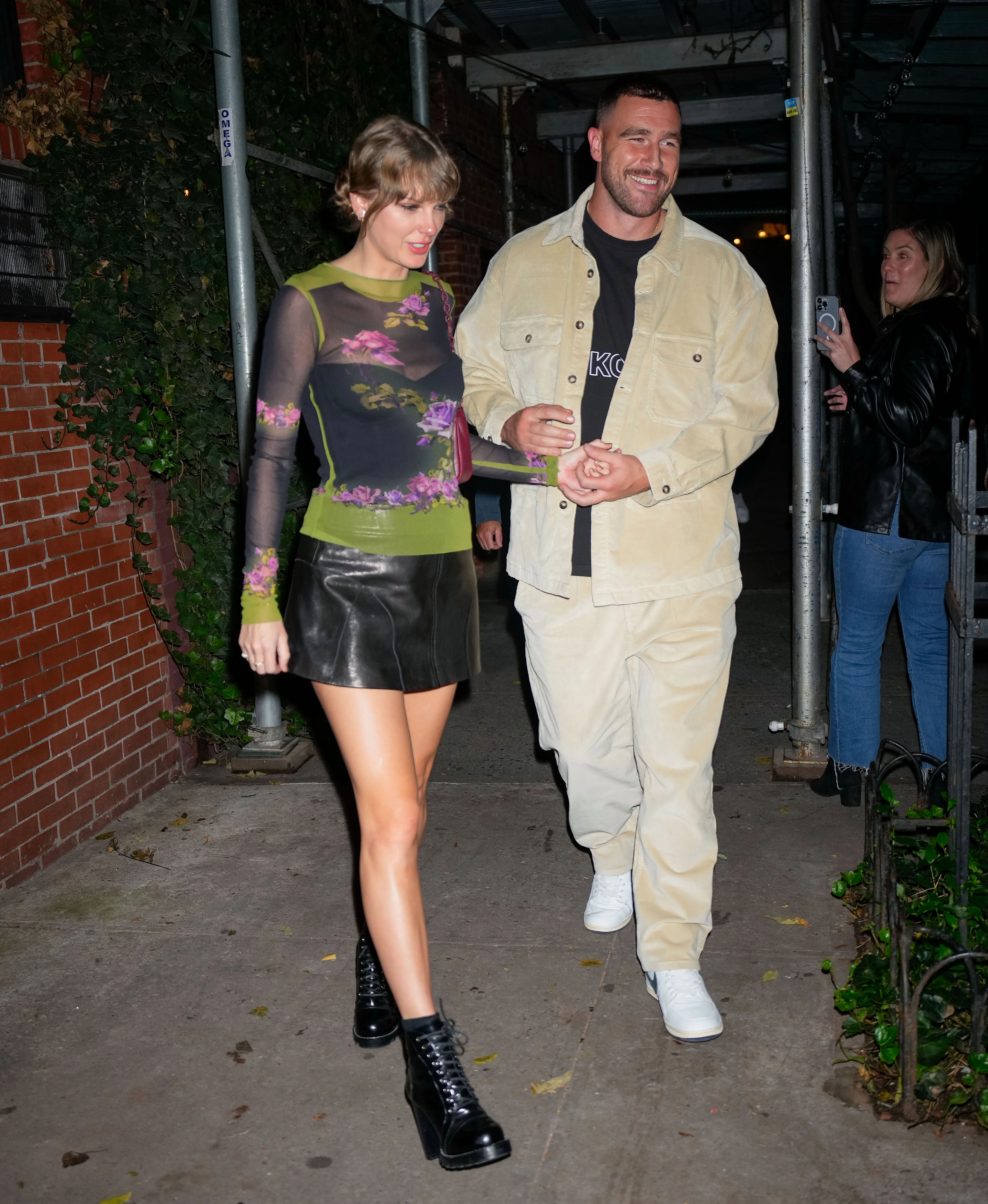 Taylor Swift and Travis Kelce walking hand-in-hand outside a restaurant.
