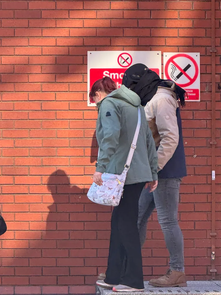 Two people walk past a red brick wall with 