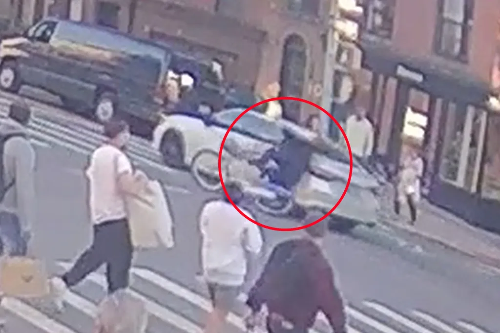An unmarked NYPD car hits a cyclist at a city intersection, with pedestrians walking nearby.
