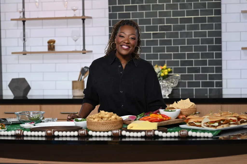 Tiffany Derry stands behind a kitchen counter filled with food, smiling at the camera.