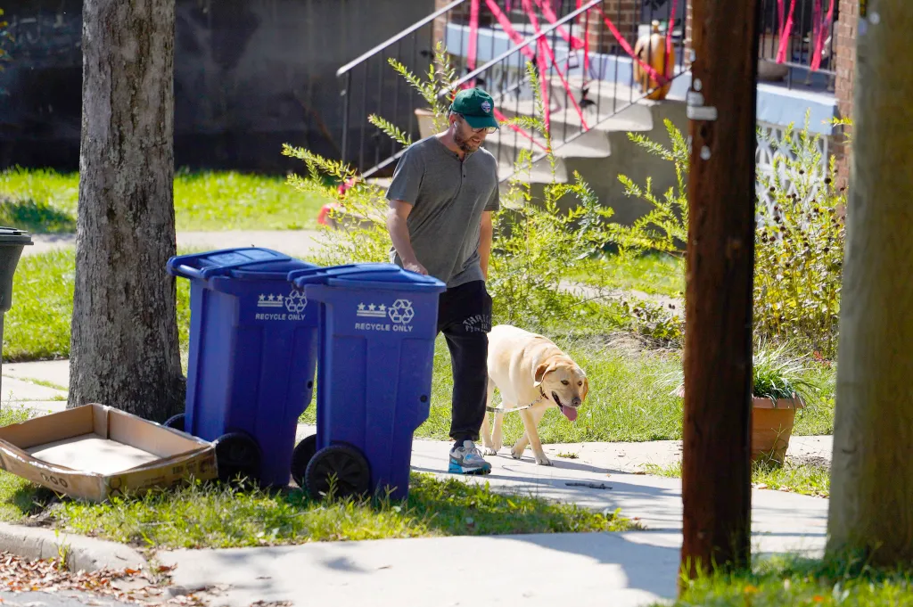 Timothy Mynett, husband of U.S. Rep. Ilhan Omar, walks his dog past two blue recycling bins outside their Washington residence.