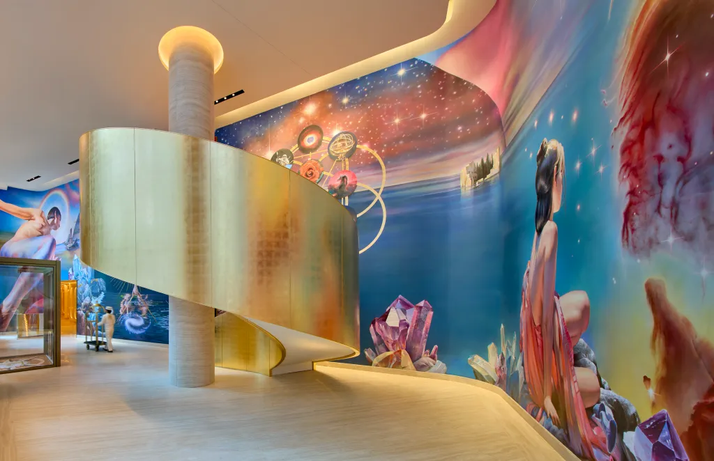 Interior view of Faena New York showing a golden spiral staircase and colorful murals on the walls.